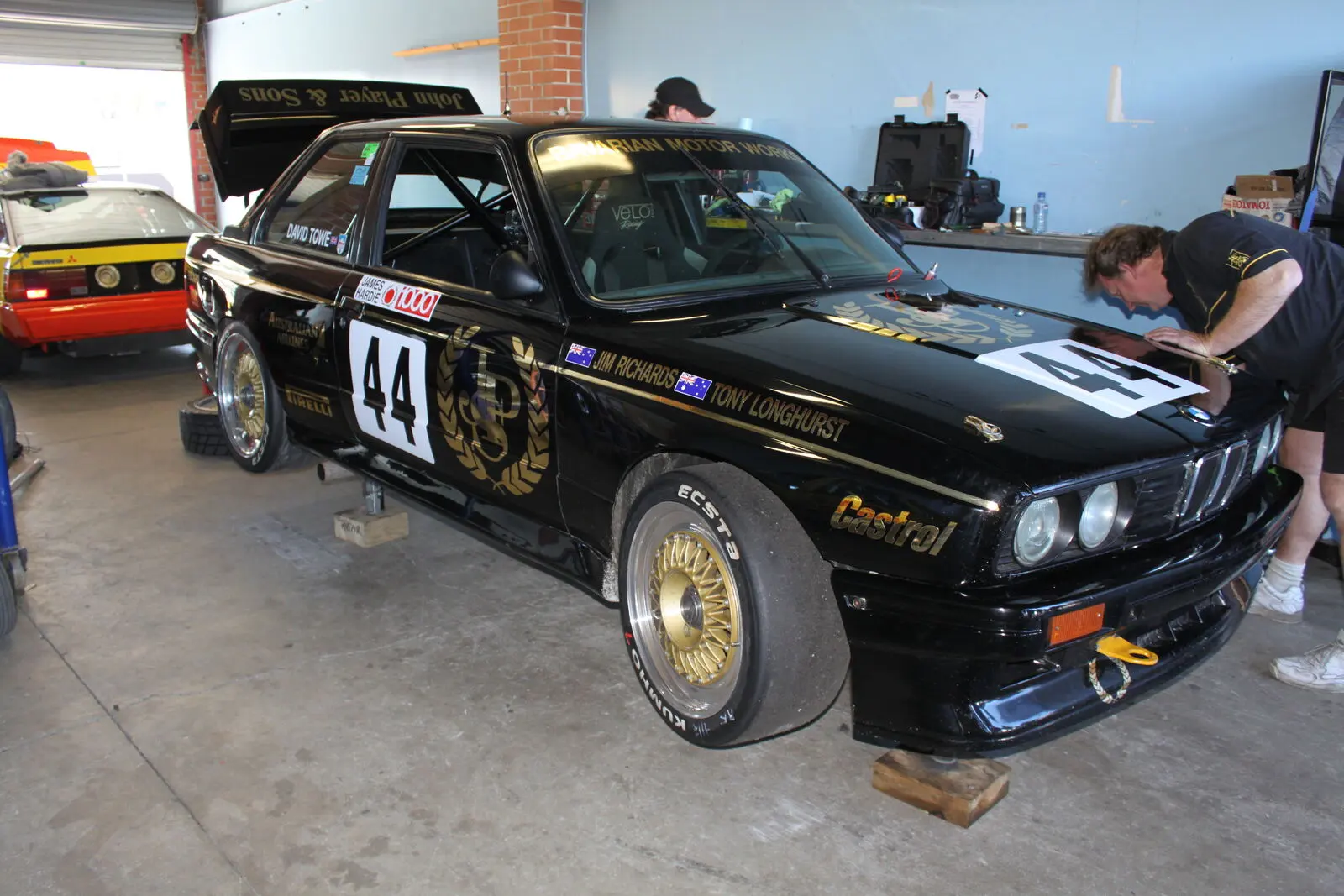 Black BMW E30 M3 race car with gold wheels in a workshop